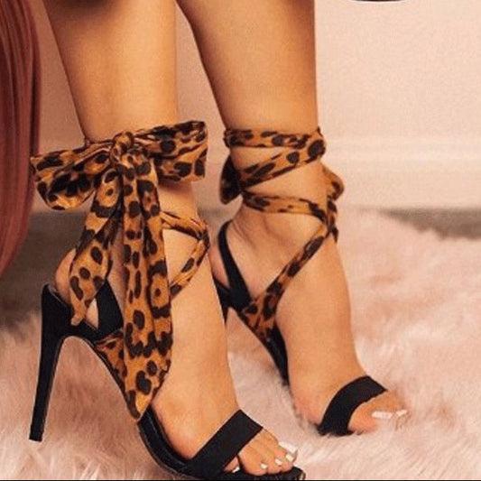 Leopard print high-heeled shoes with bow details on a soft surface.
