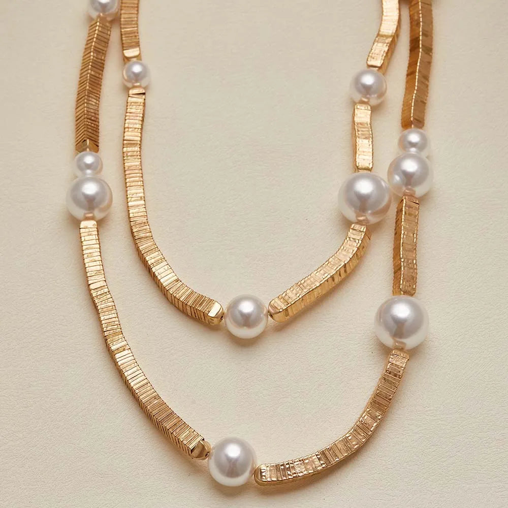 Two gold necklaces with pearls on a beige background