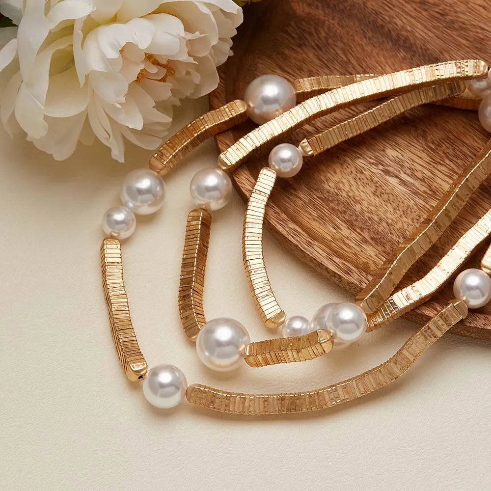 Gold bracelet with pearls on a wooden surface with a white flower.